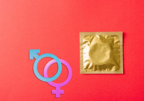 World sexual health or Aids day, Top view flat lay Male, female gender signs condom in wrapper pack, studio shot isolated on a red background, Safe sex and reproductive health concept