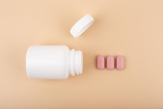 Minimal flat lay with white opened medication bottle with accurately spilled pills against neutral beige background. Concept of vitamins for pregnant or supplements 