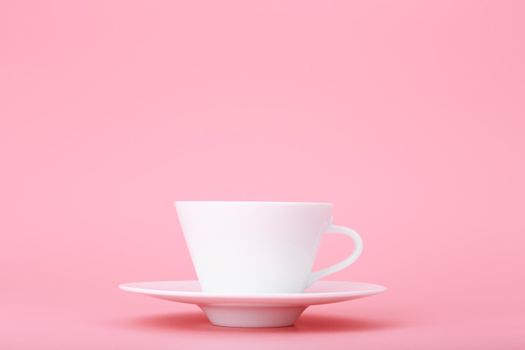 Close up of white ceramic coffee or tea cup with saucer isolated on bright pink background with copy space. Trendy concept of hot drinks and kitchenware