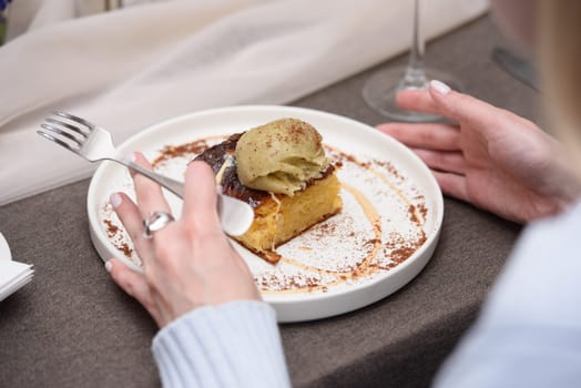 Woman eats portokalopita, greek orange cake made with shredded filo, greek yoghurt, and olive oil with vanilla ice cream. Mediterranean cuisine dessert.