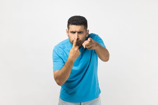 Portrait of funny unshaven man wearing blue T- shirt standing touching his nose with finger and showing lie gesture, body language. Indoor studio shot isolated on gray background.