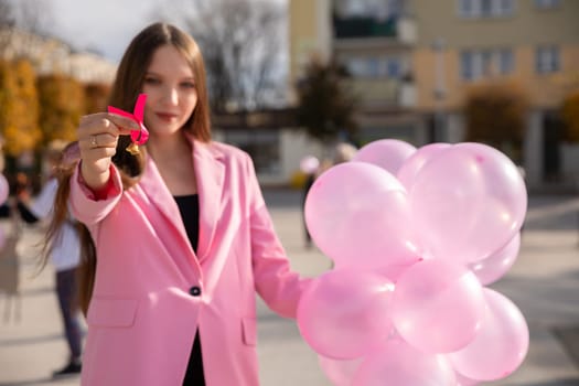 A girl holds pink balloons in one hand and a pink ribbon in the other to symbolize preventive breast examinations. Breast cancer prevention.
