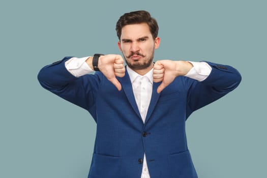 Portrait of sad displeased handsome man with mustache standing and showing dislike gesture, disagree, wearing official style suit. Indoor studio shot isolated on light blue background.