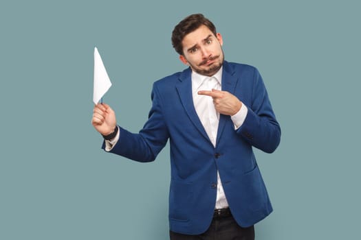 Portrait of stressed man with mustache standing and pointing at white flag, looking at camera with frowning face, wearing white shirt and jacket. Indoor studio shot isolated on light blue background.