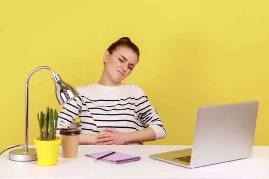 Unhappy woman office manager sitting at workplace, feeling discomfort and abdominal cramps, suffering heartburn or dysmenorrhea. Indoor studio studio shot isolated on yellow background.