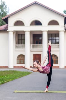 Dancer pose. Full length portrait of slim woman with ponytail wearing sportswear practicing yoga outdoor, doing Natarajasana exercise on one leg, stretching muscles and balancing.