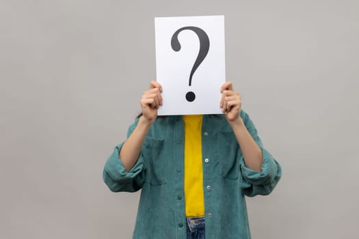 Portrait of unknown woman covering face with question mark, finding smart solution, asking for advice, wearing casual style jacket. Indoor studio shot isolated on gray background.