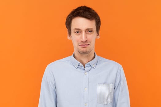 Portrait of unhappy sad depressed man standing looking at camera, being in bad mood, expressing sadness and sorrow, wearing light blue shirt. Indoor studio shot isolated on orange background.