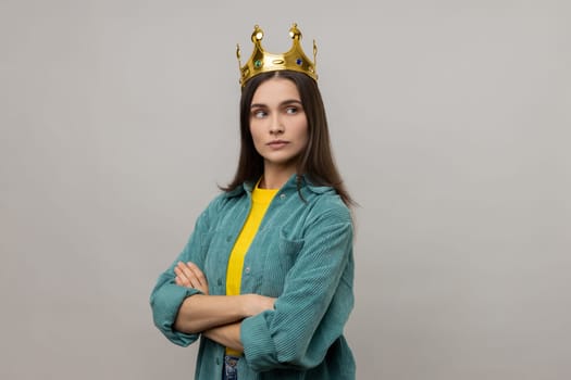 Woman with crown on head, standing with crossed arms, self confidence in success, self-motivation and dreams to be best, wearing casual style jacket. Indoor studio shot isolated on gray background.