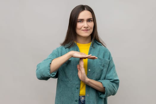 Portrait of stressed young adult woman showing time out gesture, looking with nervous expression, deadline, wearing casual style jacket. Indoor studio shot isolated on gray background.