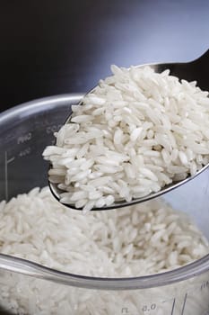 Rice grains in a spoon on a wooden background