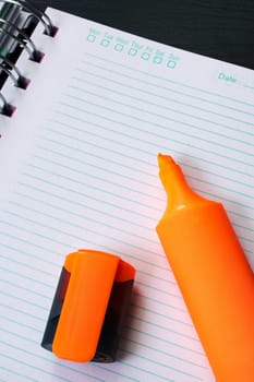 Orange marker and notebook on a black wooden table