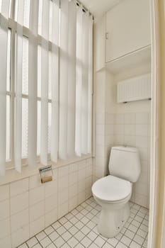 a white toilet in a bathroom with windows on the wall and tiled floor below it is an open shower stall