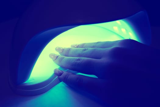 Girl's hand inside an ultraviolet lamp for drying nail polish close-up. Color toning applied