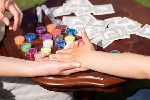 Kid's animator is creating a Shimmering sparkling glitter tattoo on a child's hand at a birthday party. Body art