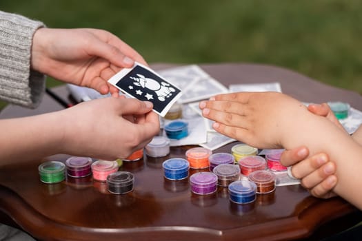 Kid's animator is creating a Shimmering sparkling glitter tattoo on a child's hand at a birthday party. Body art