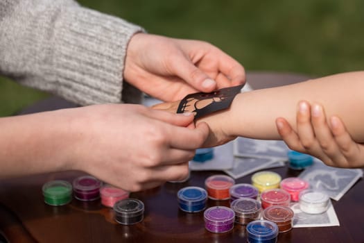 Kid's animator is creating a Shimmering sparkling glitter tattoo on a child's hand at a birthday party. Body art