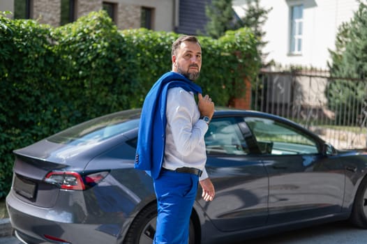 Attractive bearded man in a blue suit near a black car in the countryside in summer