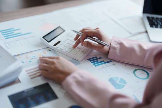 businesswoman or accountant working on calculator and laptop computer to calculate business data during using accountancy document at office.