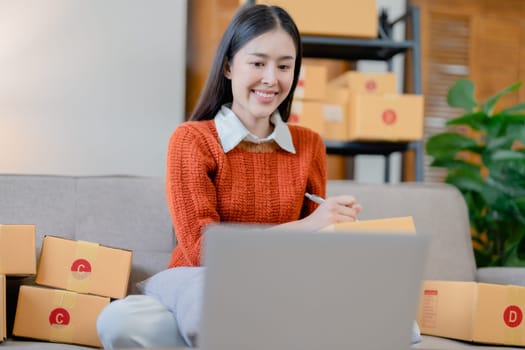 Starting small business entrepreneur of independent young Asian woman online seller is using computer and taking orders to pack products for delivery to customers. SME delivery concept.