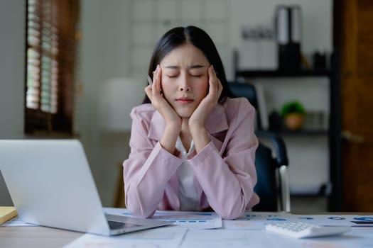 Portrait of a young Asian woman showing acute headache from sitting for a long time at work