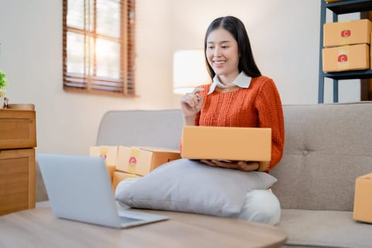 Starting small business entrepreneur of independent young Asian woman online seller is using computer and taking orders to pack products for delivery to customers. SME delivery concept.