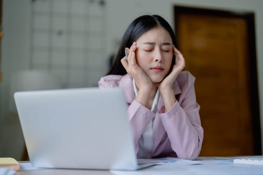 Portrait of a young Asian woman showing acute headache from sitting for a long time at work