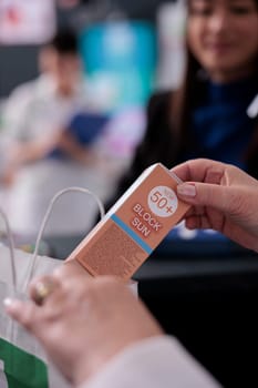 Pharmacy cashier selling sunblock lotion and putting product in buyer shopping bag. Medical retail store seller holding sunscreen, throwing cosmetology sun protection cream in paper package close up