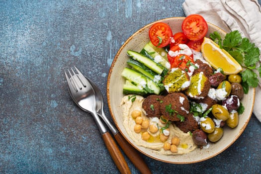 Falafel salad bowl with hummus, vegetables, olives, herbs and yogurt sauce. Vegan lunch plate top view on rustic stone background, healthy meal with falafel and veggies, space for text