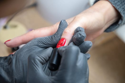 A master manicurist covers the renewed nails of the client with red varnish, Manicure process in beauty salon, High quality photo