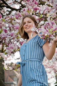 blonde with pleasure inhales an aroman of magnolia flowers standing under a tree. High quality photo