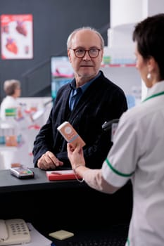Old man in glasses waiting for drugstore cashier scanning product to pay. Young woman pharmaceutical worker using scanner on sunblock lotion barcode, selling medications to client