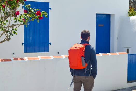 Traveler with a red backpack near beauty house at a Greece