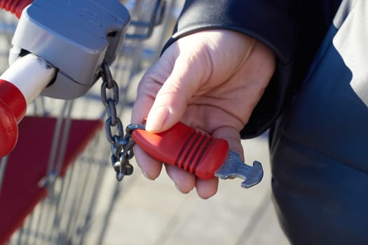 A woman's hand holds a metal lock from a shopping cart. On the street during the day.