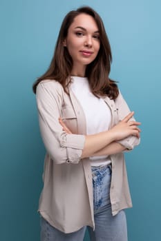 romantic brunette 30 year old female person dressed in a shirt and jeans looks at the camera on a blue background.