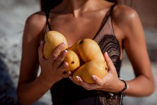 Yellow mango in the hands of a woman in a swimsuit.