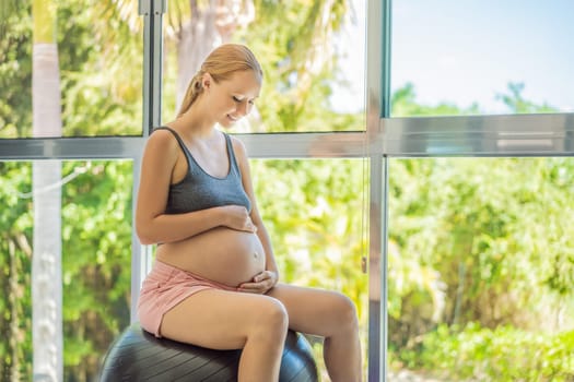 Pregnant woman exercising on fitball at home. Pregnant woman doing relax exercises with a fitness pilates ball. Against the background of the window.