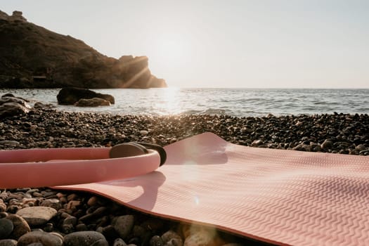 Young woman with long hair in white swimsuit and boho style braclets practicing outdoors on yoga mat by the sea on a sunset. Women's yoga fitness routine. Healthy lifestyle, harmony and meditation