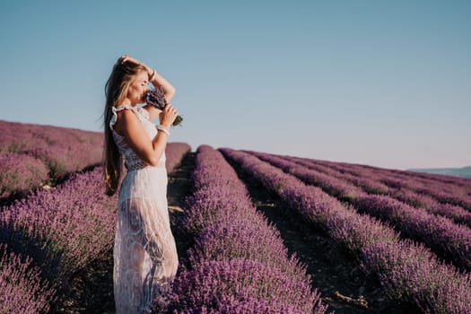 Close up portrait of young beautiful woman in a white dress and a hat is walking in the lavender field and smelling lavender bouquet.