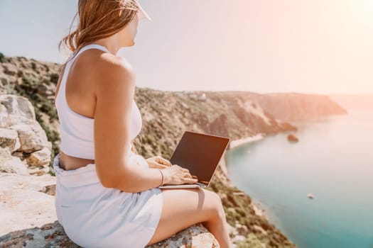 Digital nomad, Business woman working on laptop by the sea. Pretty lady typing on computer by the sea at sunset, makes a business transaction online from a distance. Freelance remote work on vacation