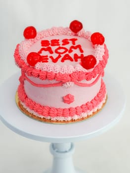 frosted pink red cake for mothers day celebration with funny text topping best mom evah on white studio background