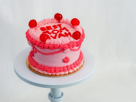 frosted pink red cake for mothers day celebration with funny text topping best mom evah on white studio background