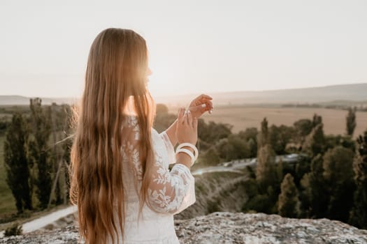 Romantic beautiful bride in white dress posing with sea and mountains in background. Stylish bride standing back on beautiful landscape of sea and mountains on sunset