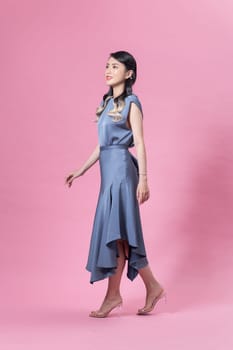 Pretty stylish girl with long curly hair wearing beautiful blue dress and posing against pink background