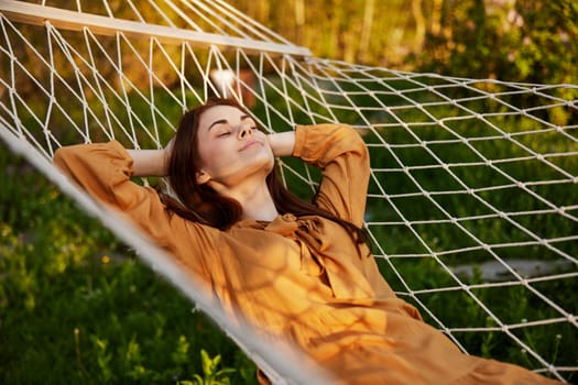 a happy woman is resting in a hammock with her eyes closed and her hands behind her head smiling happily enjoying the day. High quality photo