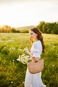 vertical portrait of a beautiful woman in a light dress with a basket full of daisies in nature. High quality photo