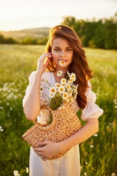 cute, happy woman with a basket of flowers in nature holds a camomile in her mouth. High quality photo