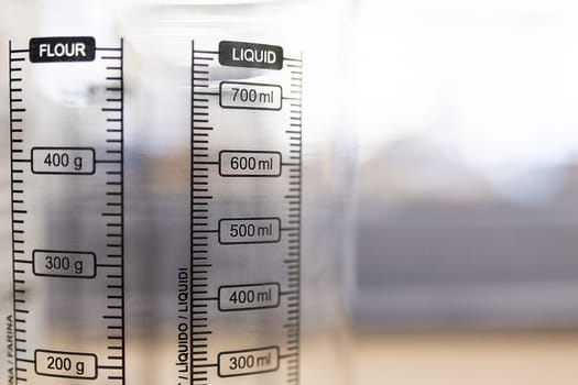 Close-up on a transparent measuring jug with scales for flour and liquid, selective soft focus.