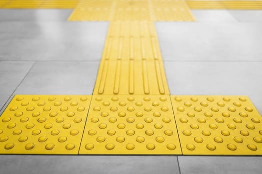 Top view of yellow tactile tiles for the blind stacked on gray tiled floor.