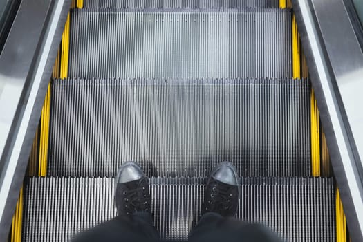 Top view of the legs in sneakers standing on the escalator step.